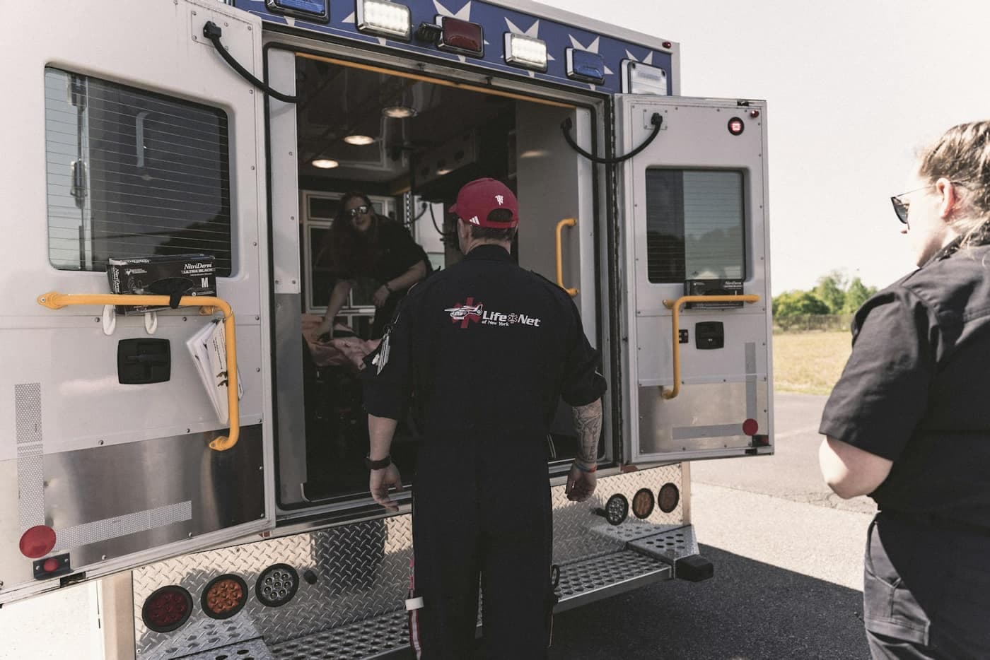 Three crew members in uniform at the open rear doors of an ambulance.